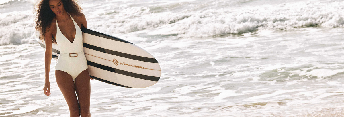 Mulher de maio branco carregando prancha de surf na beira do mar